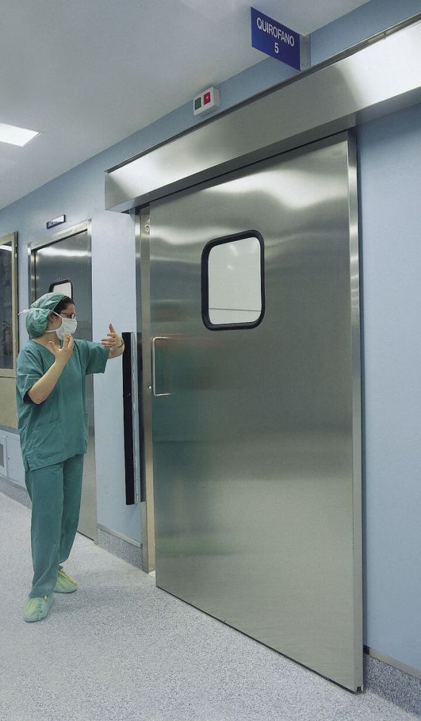Mitarbeiterin steht vor leichtgeöffneter OP-Tür.