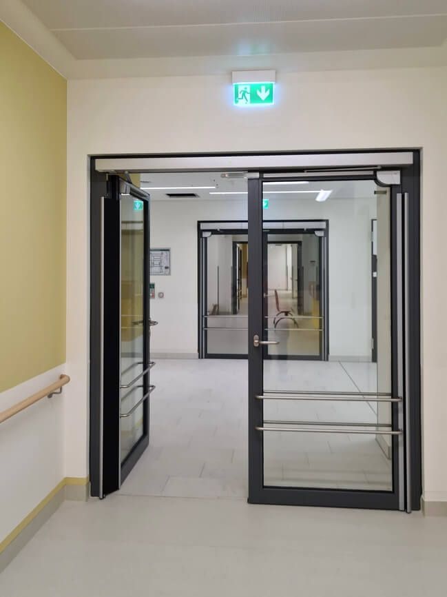 Automatische Drehflügeltür in einem Krankenhaus, Flügel auf linke Seite geöffnet mit Blick in den Flur.