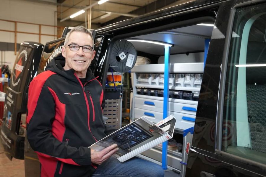 Mitarbeiter lächelt während der Servicearbeiten in die Kamera und hält ein Buch in der Hand.